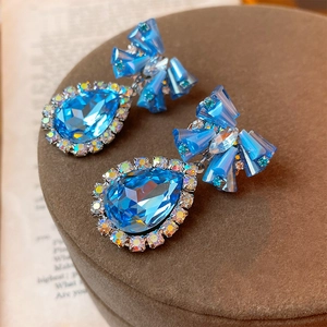 Detailed close-up of blue teardrop crystal earrings with rhinestone bow on display