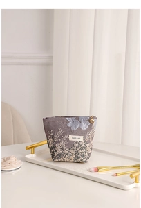 Detail of floral jacquard makeup bag with golden flower zipper on a white tray