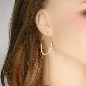 Close-up of a model wearing large golden round hollow hoop earrings in stainless steel