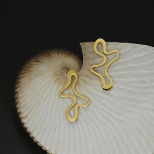 Macro view of abstract wavy gold earrings on seashell with polished metal texture