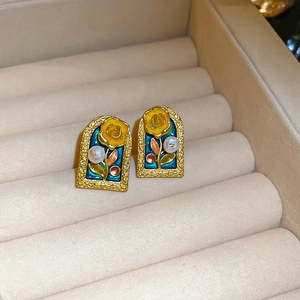 Macro view of vintage gold earrings with blue enamel, yellow rose and pearls on velvet tray