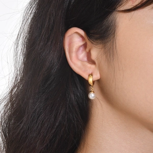 Macro shot of gold knot earrings with round white pearl charm on model ear