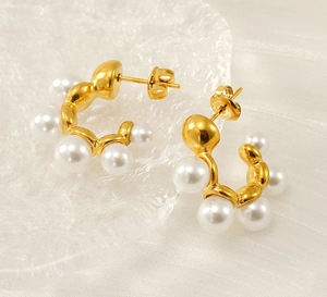 Detail view of French vintage C-shaped gold pearl earrings on elegant textured glass