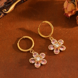 Boucles d'oreilles fleur dorées avec strass roses sur un fond artistique vintage