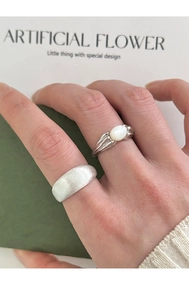 Macro detail of a brushed silver wide band and vintage style ring with white oval stone
