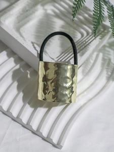 Detail of gold hammered texture metal buckle on a black elastic hair tie with greenery