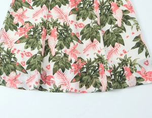 Détail de l'imprimé floral et perroquet tropical sur robe en mousseline blanche et ourlet