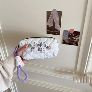 Detailed embroidery of cat and floral patterns on white quilted fabric pouch with purple strap