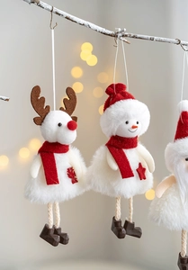 Detail of plush Christmas elk and snowman ornaments hanging on snowy pine branches