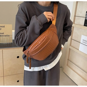 Detailed view of brown woven chest bag with adjustable strap worn by a model
