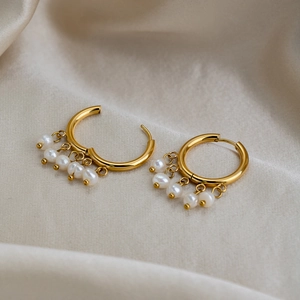 Macro view of 18K gold-plated hoop earrings with freshwater pearl tassels on white silk