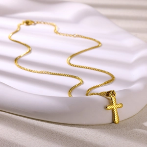 Detail of 18K gold stainless steel cross pendant on a white wavy jewelry display tray