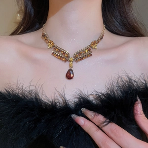 Detail of a gold necklace with wing patterns and a teardrop red gemstone on model