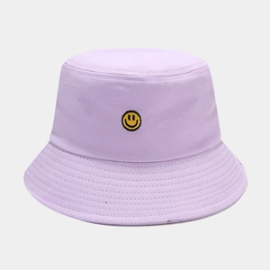 Detail of yellow smiley face embroidery on a lavender canvas bucket hat with dense stitching