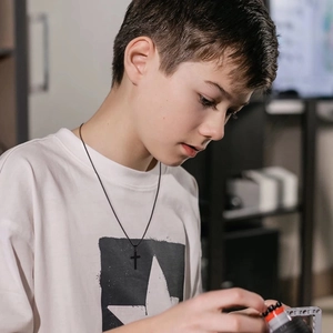 Close-up of a boy wearing a black double-layered stainless steel cross necklace on a white tee
