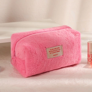 Close-up of a soft pink plush cosmetic bag with a decorative embroidered fabric label
