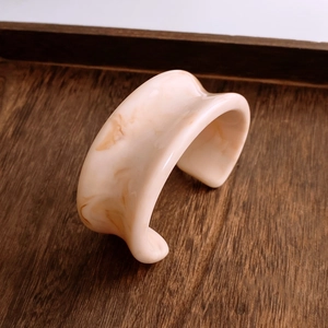 Dettaglio del bracciale rigido in resina con trama marmorizzata crema su legno