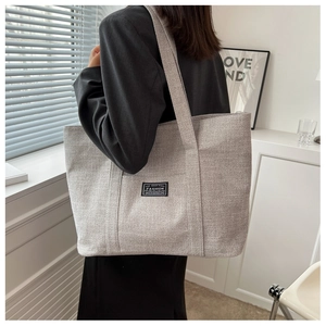Model wearing a light grey linen tote bag with black straps in a minimalist indoor setting