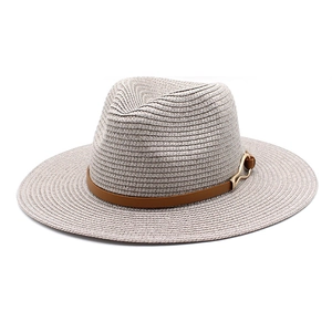 Close-up of wide brim straw fedora featuring a brown leather band and gold buckle detail