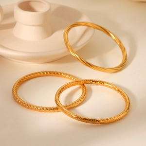Three textured gold stainless steel bracelets with rope and hammered designs on ceramic stand
