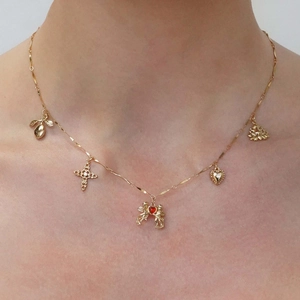 Detail view of a gold chain necklace with heart, cross, and cupid pendants on a model