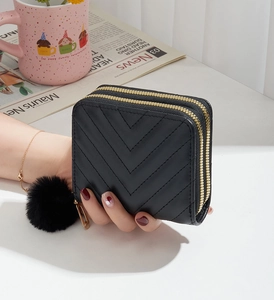 Detail of a black quilted wallet with V-stitch design and a soft fur ball keychain accessory