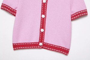 Close-up of pink knit cardigan featuring red ribbed edges and white contrast stitching