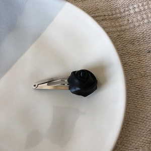 Close-up of black PU leather rose hair clip with silver metal bow on a white plate