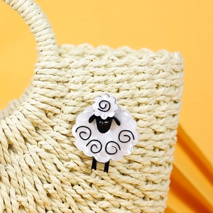 Handmade acrylic sheep brooch in black and white pinned on a stylish straw bag