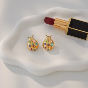 Chic ladybug stud earrings in gold with colorful rhinestones on a white ceramic tray