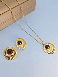 Macro view of gold pendant and earrings with blue gems and radial texture details
