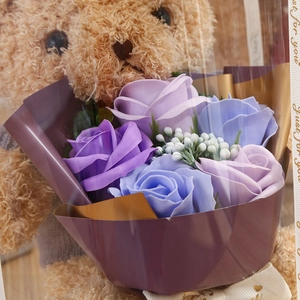 Close-up of a brown teddy bear and purple soap flower bouquet in a romantic gift box