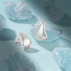 Macro shot of silver C-shaped teardrop stud earrings on blue crystals background