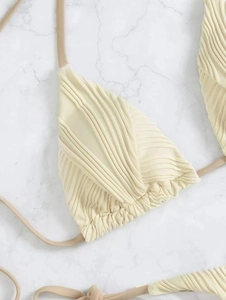 Dettaglio del top bikini giallo crema a costine con coulisse su sfondo in marmo