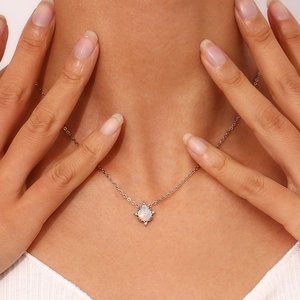 Close-up detail of dainty stainless steel necklace with teardrop opal pendant and micro-set stones.