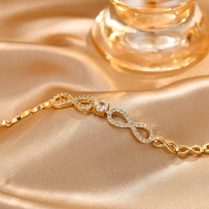 Makrodetail eines goldenen Infinity-Armbands mit weißen Zirkonia auf Seidenstoff