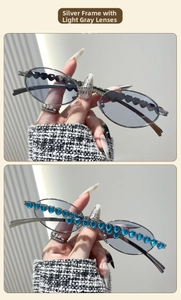 Detail of silver oval sunglasses with heart-shaped blue gemstone accents and gray lenses