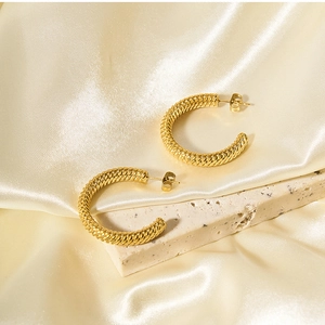 Macro shot of gold-plated stainless steel C-shaped earrings with spiral texture on satin