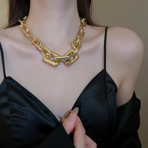 Close-up of a chunky gold link chain necklace with a geometric clasp on a model
