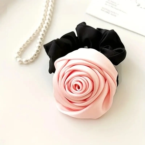 Detailed view of pink satin rose scrunchie with black elastic band on elegant white surface
