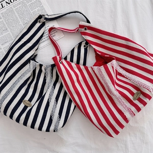 Détail du sac cabas rayé avec dentelle et logo métallique sur tissu blanc