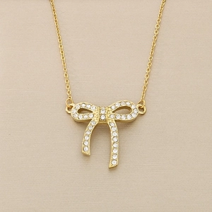 Macro view of gold bow pendant with sparkling rhinestones on stainless steel chain
