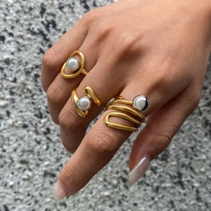 Detailed view of layered gold rings with pearls and silver beads on a stone surface