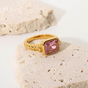 Macro detail of twisted gold ring with rectangle pink zircon on textured stone base