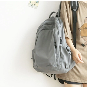 Side view of a minimalist grey nylon backpack worn by a model against a white wall