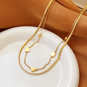 Double-layer gold snake chain necklace featuring heart pendants on white ceramic plate