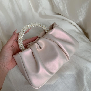 Detail of pink pearl-handle cloud bag with pleated design held against white fabric
