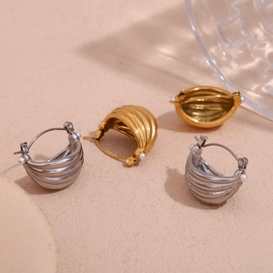 Close-up of titanium earrings with gold finish, pearl accents and wavy texture