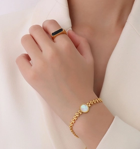 Detail of gold wheat chain bracelet with white shell heart and black inlay ring on model