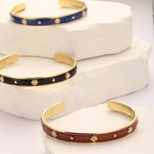 Detailed view of three enamel star-embossed gold-plated stainless steel bangles